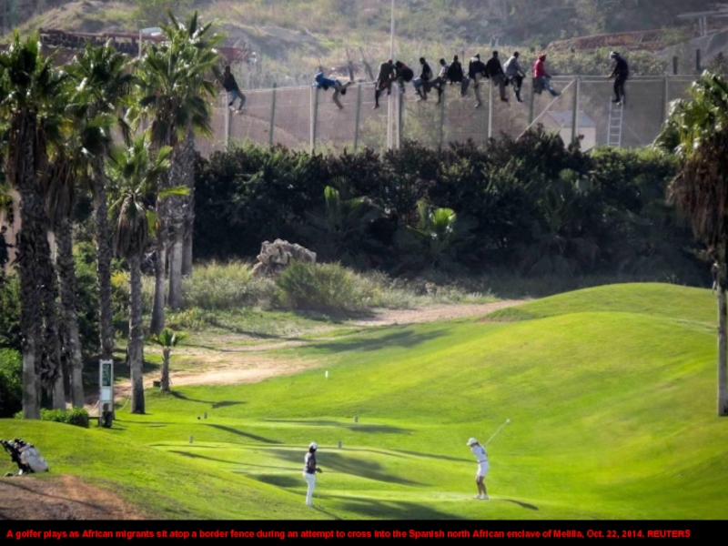 A golfer plays as African migrants sit atop a border fence
