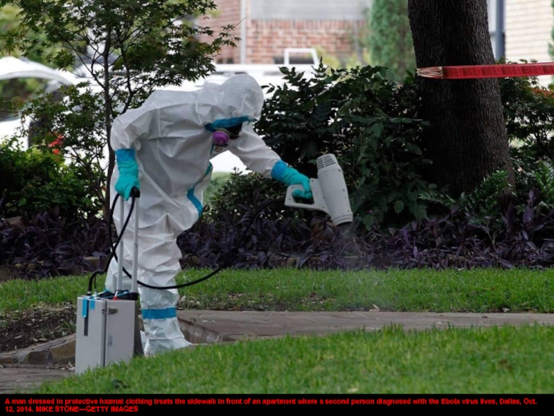 A man dressed in protective hazmat clothing treats the sidewalk in